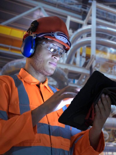An inspector holding a tablet and wearing a hard hat