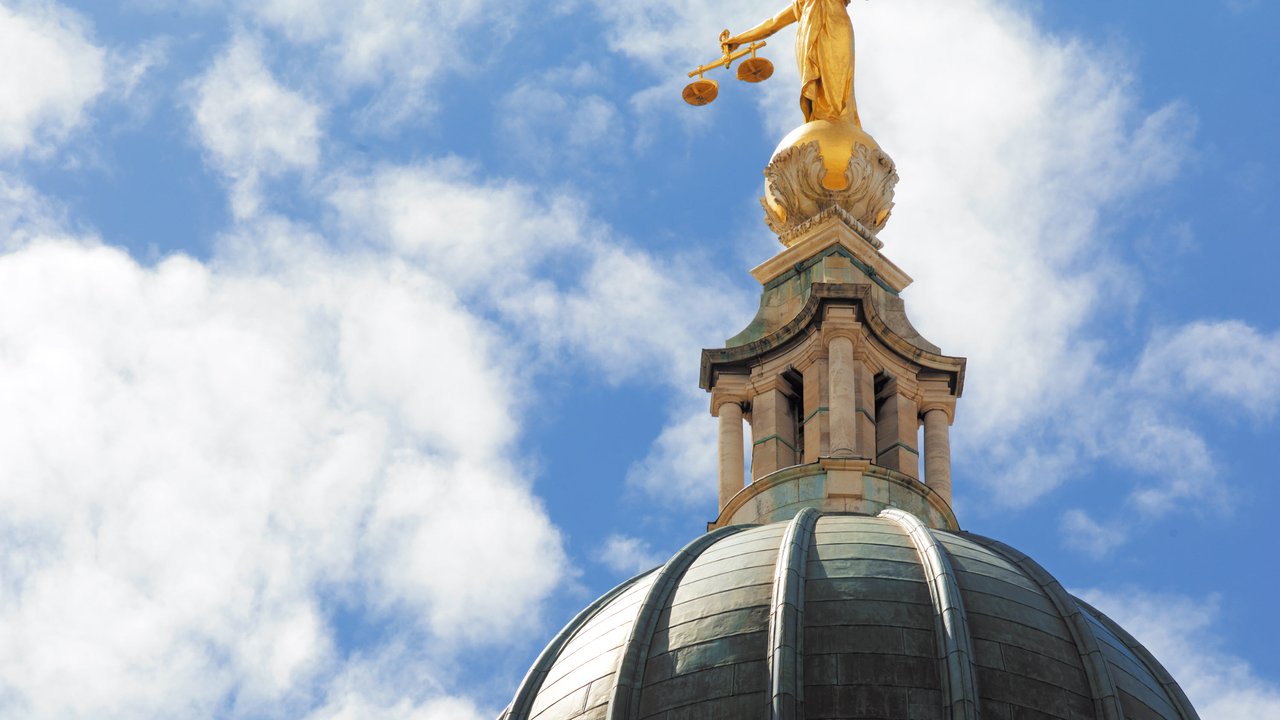 A golden statue of Lady Justice atop a dome under a blue sky with clouds.