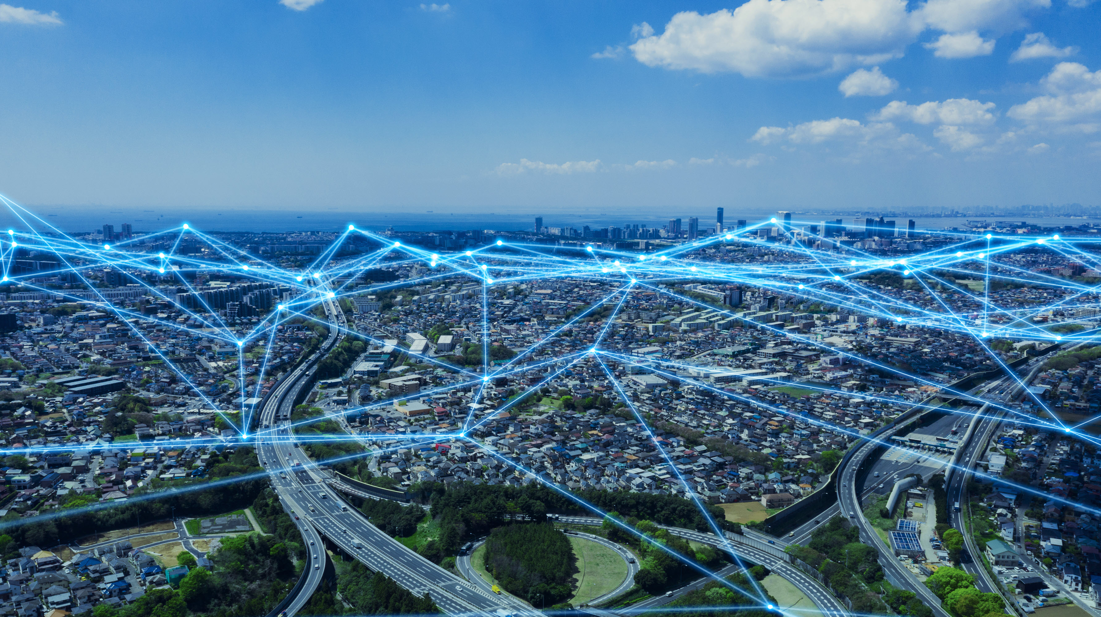 Aerial view of a city with roads and buildings, overlaid with blue network lines representing connectivity.