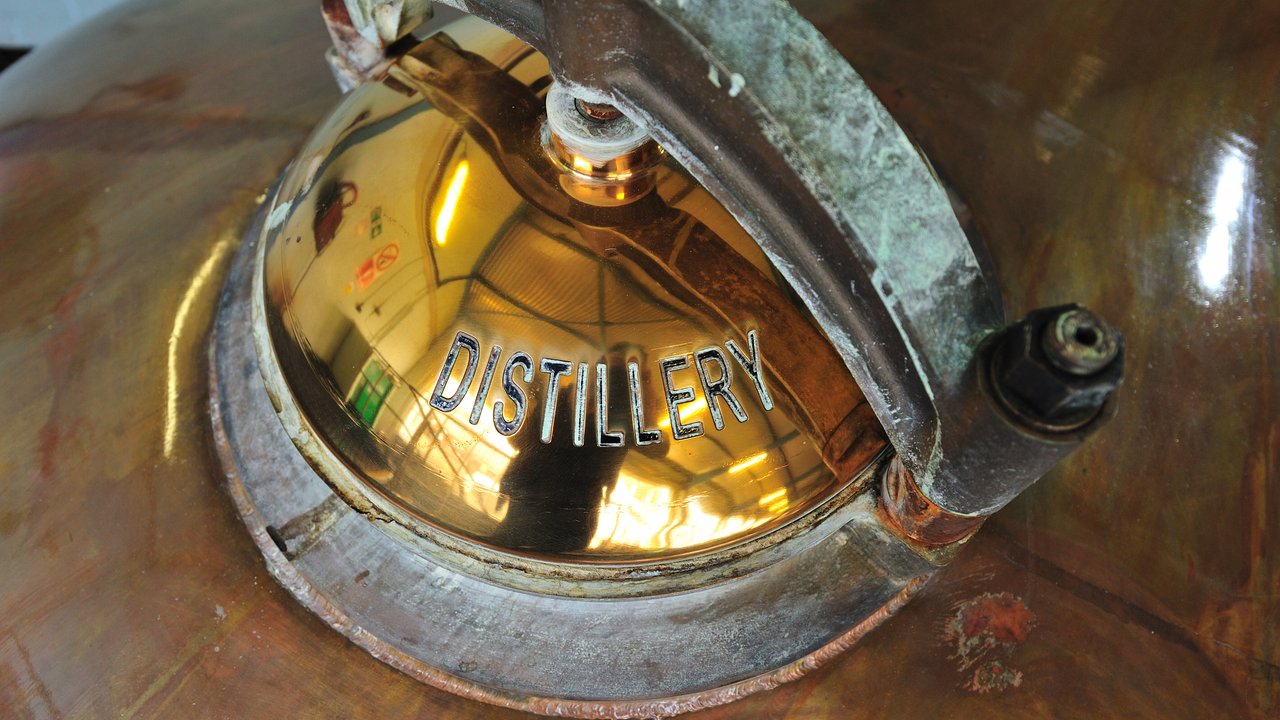Close-up of a distillery copper pot still with a shiny lid labeled "DISTILLERY".