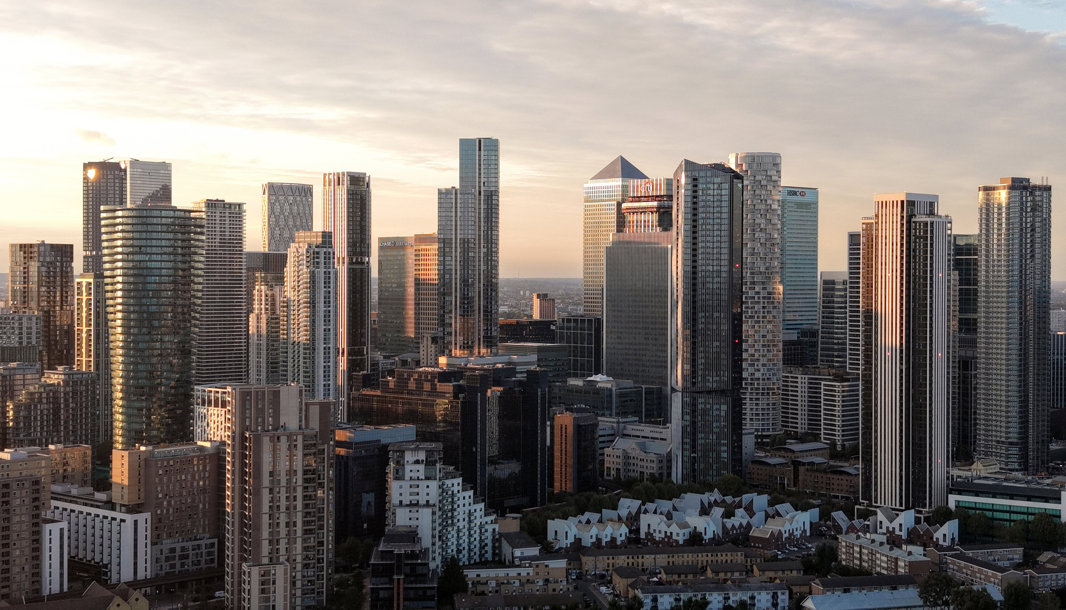 A skyline view of tall modern buildings under a cloudy sky during sunset.
