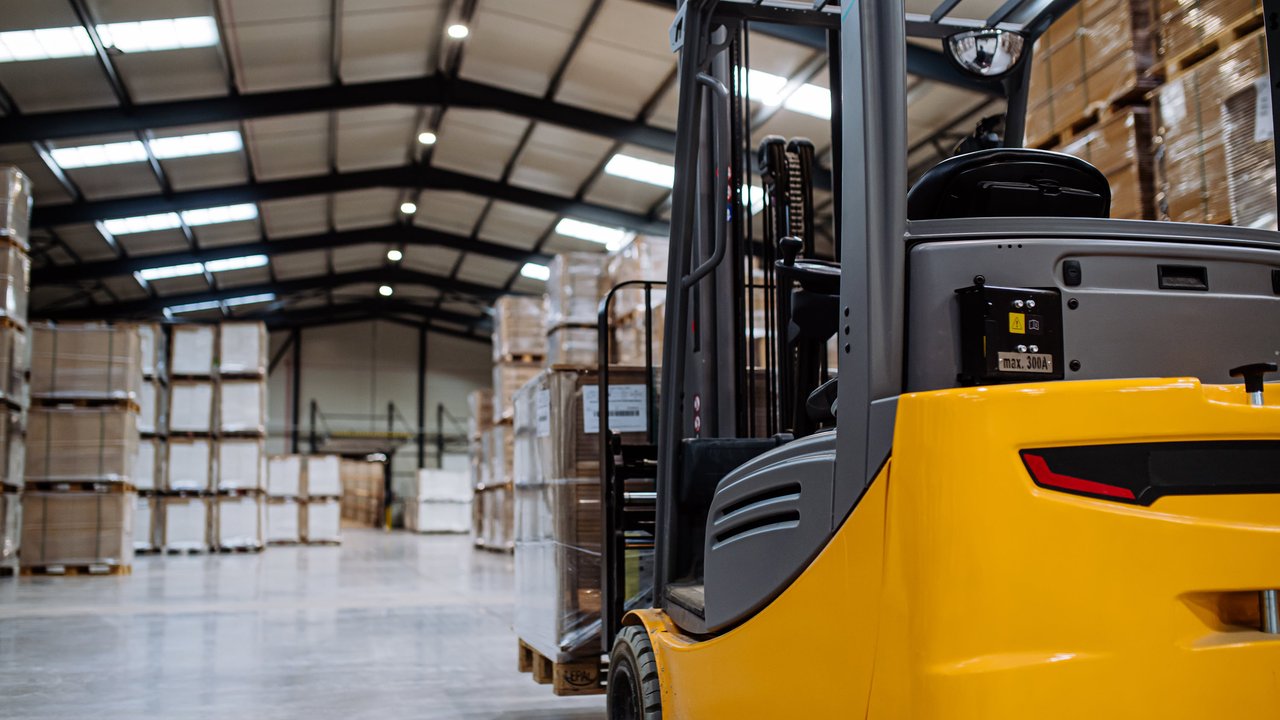 A yellow forklift is parked in a spacious warehouse filled with stacked pallets and boxes.