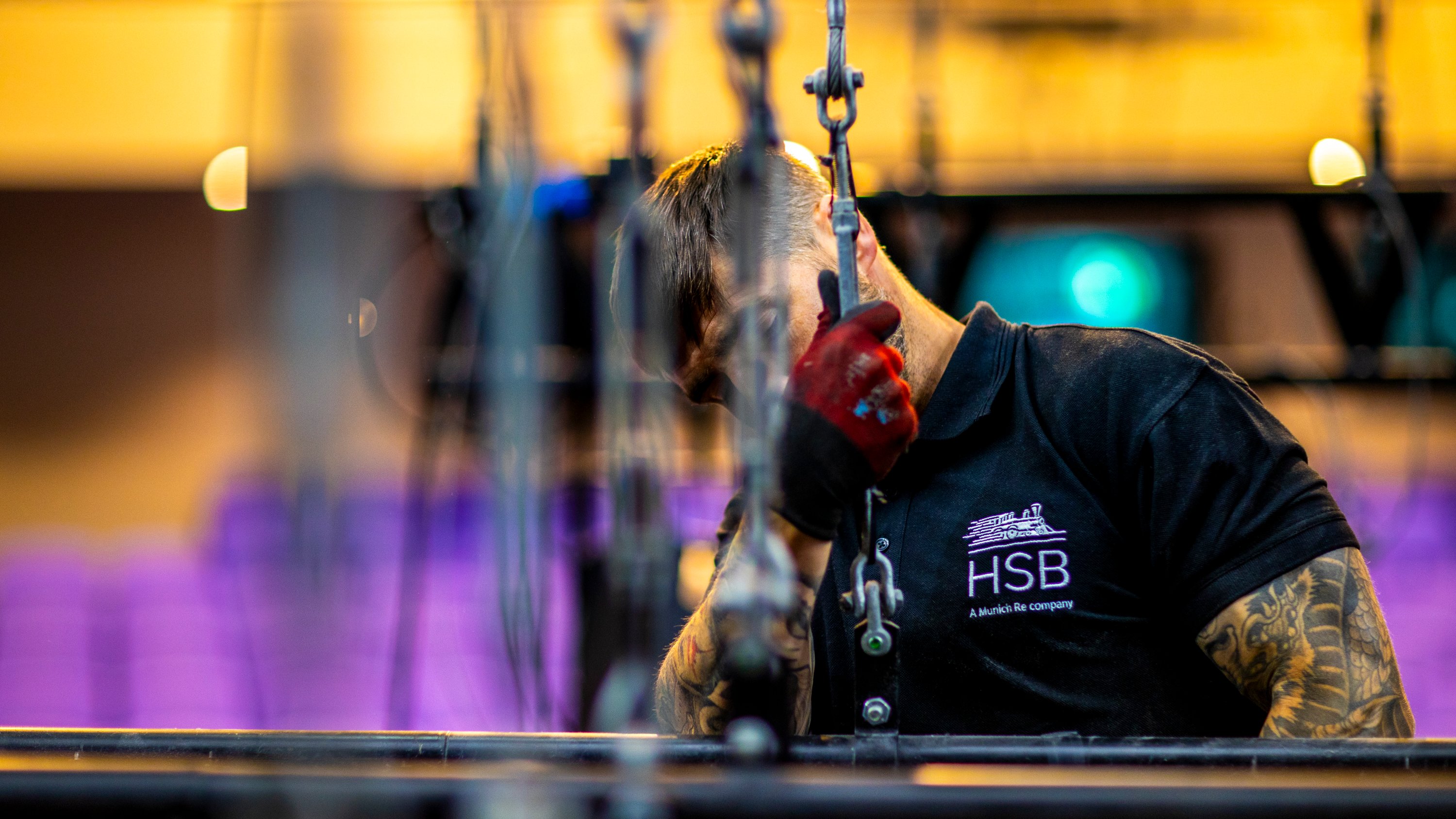 A worker in a black shirt adjusts chains in a venue with purple seating in the background.
