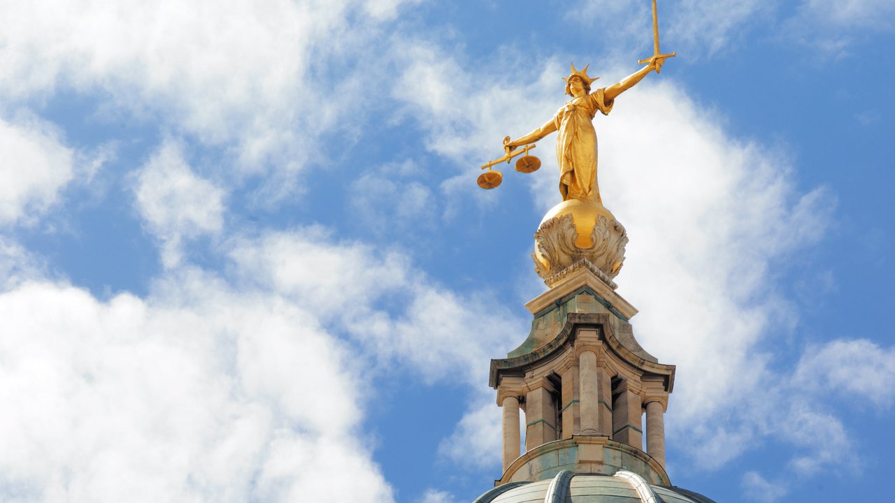 A golden statue of Lady Justice atop a dome under a blue sky with clouds.