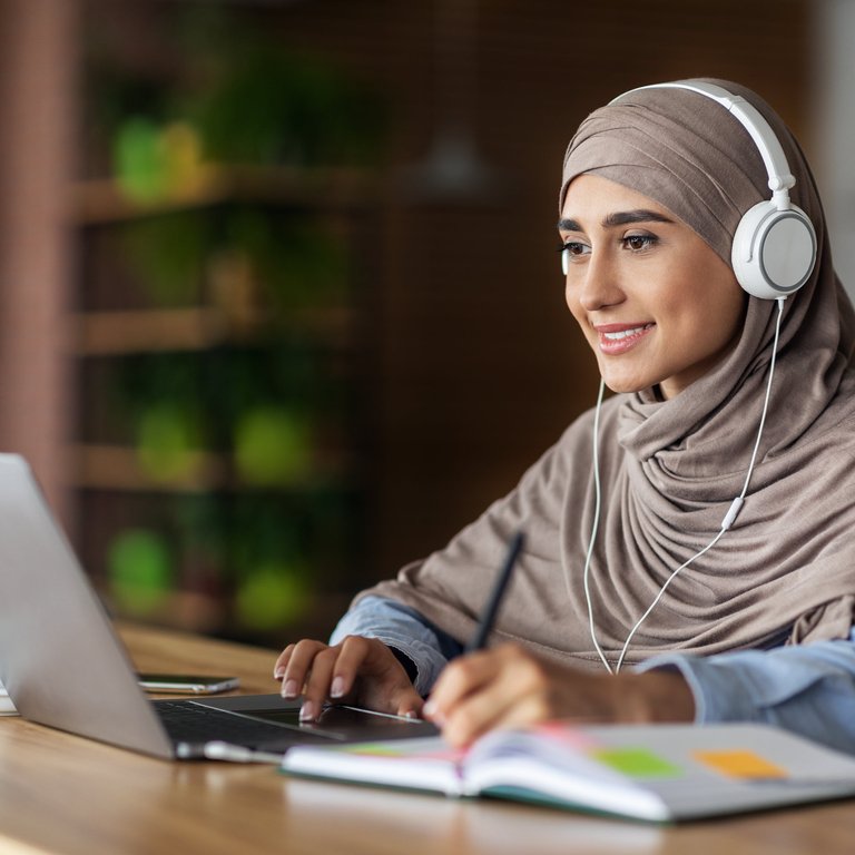 A woman using a laptop whilst wearing headphones