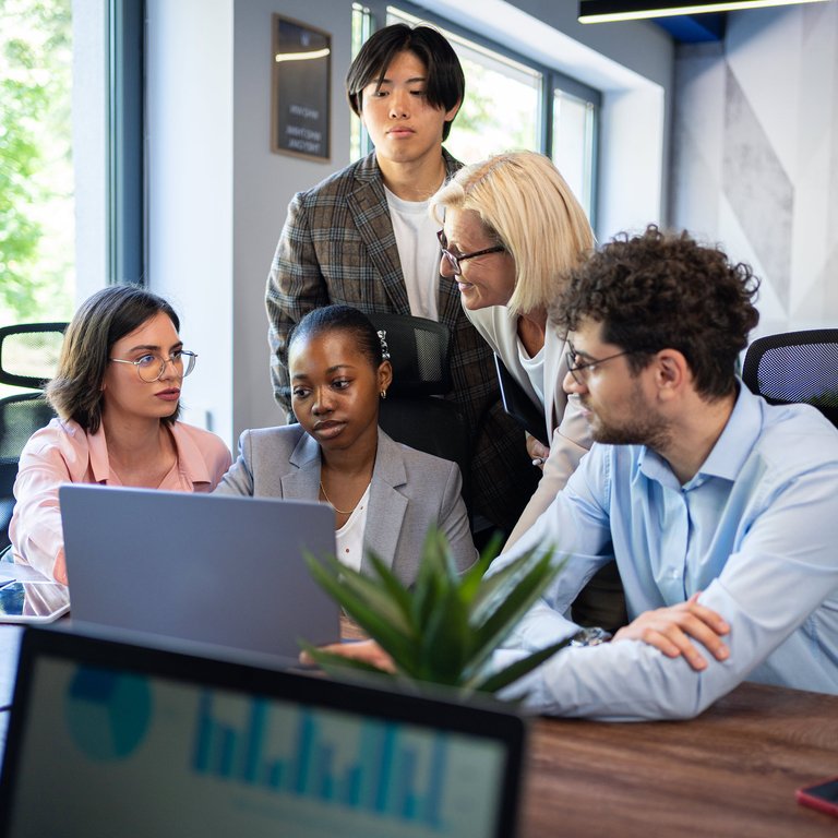 A number of office workers gathered around a laptop.