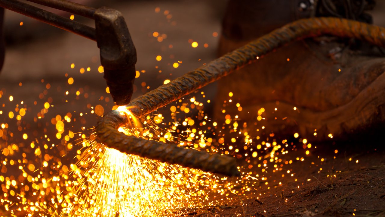 A close-up of a welding torch creating sparks near a metal rod and a work boot on the ground.