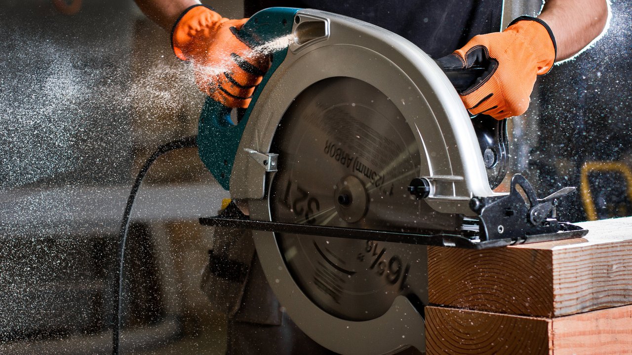 A person using a circular saw on a wooden beam, with sawdust flying in the air.