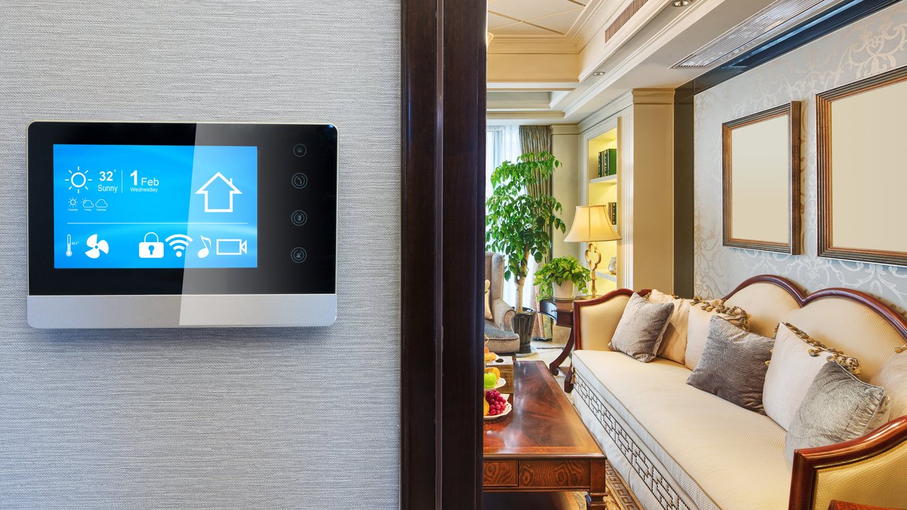 A digital control panel displays weather and date, next to a living room with a sofa, lamp, and plants.