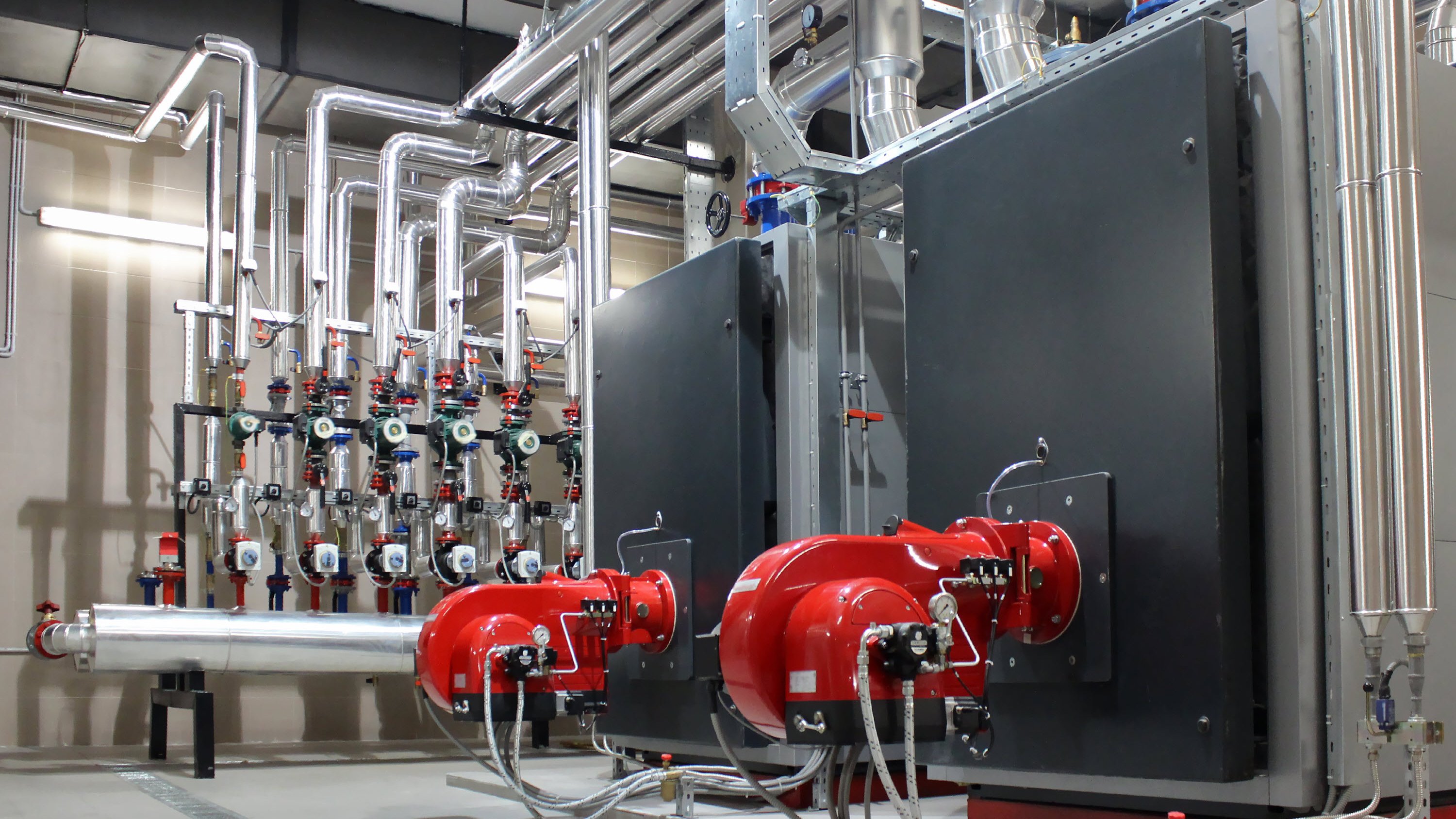 Industrial equipment with red valves, pipes, and control panels in a mechanical room.
