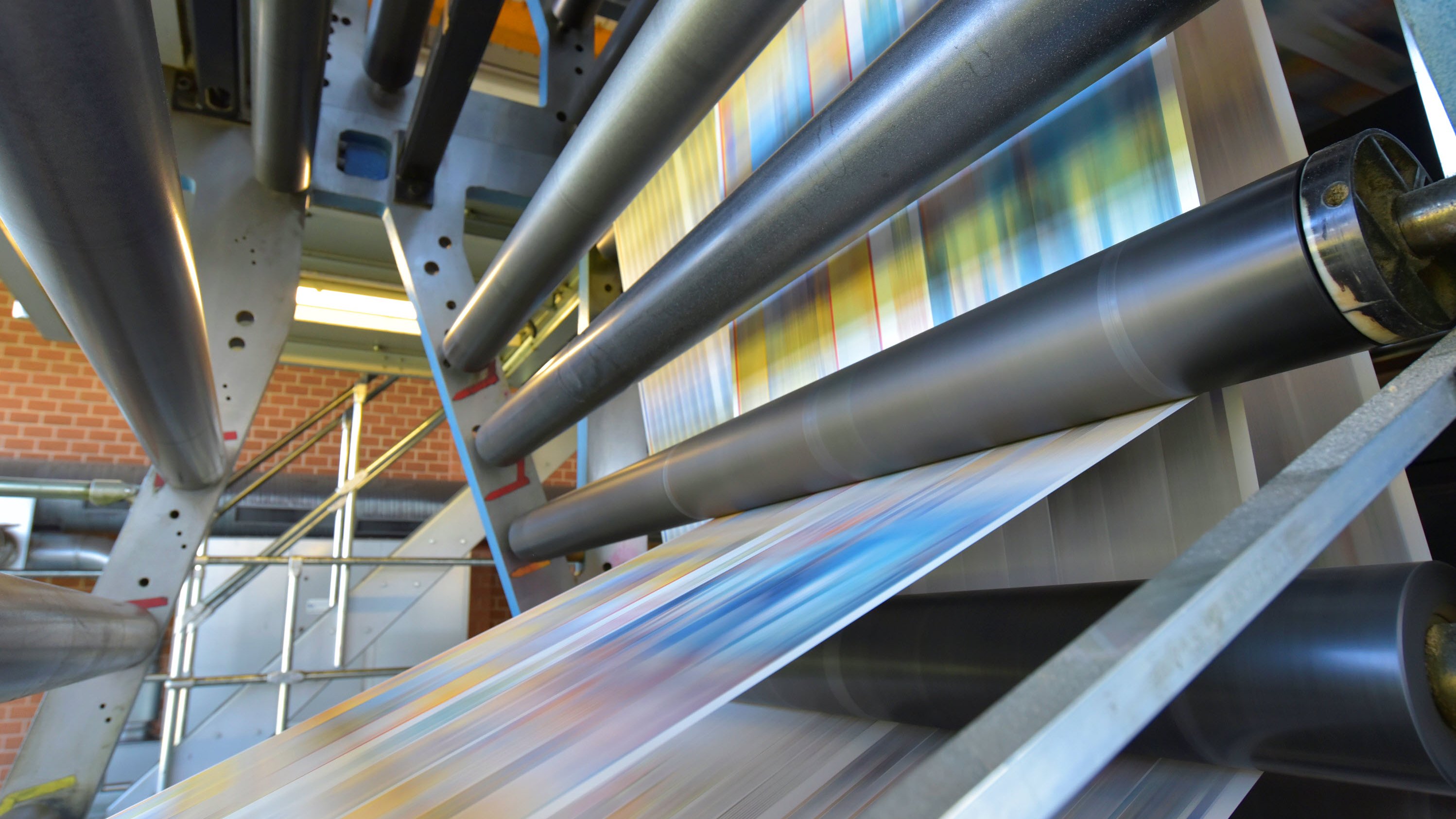 Printing press with colorful sheets emerging from rollers in a factory setting.