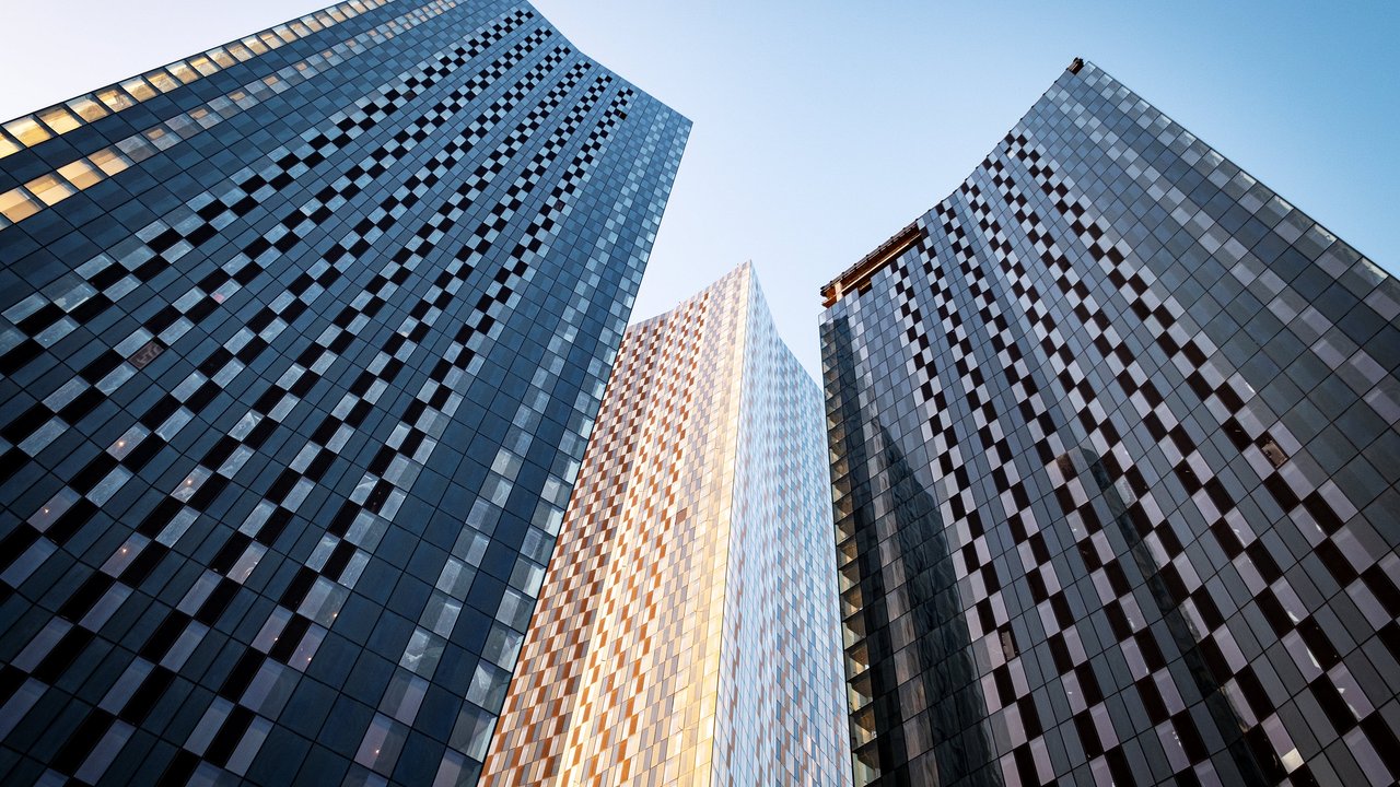 Three tall glass skyscrapers viewed from below against a clear blue sky.