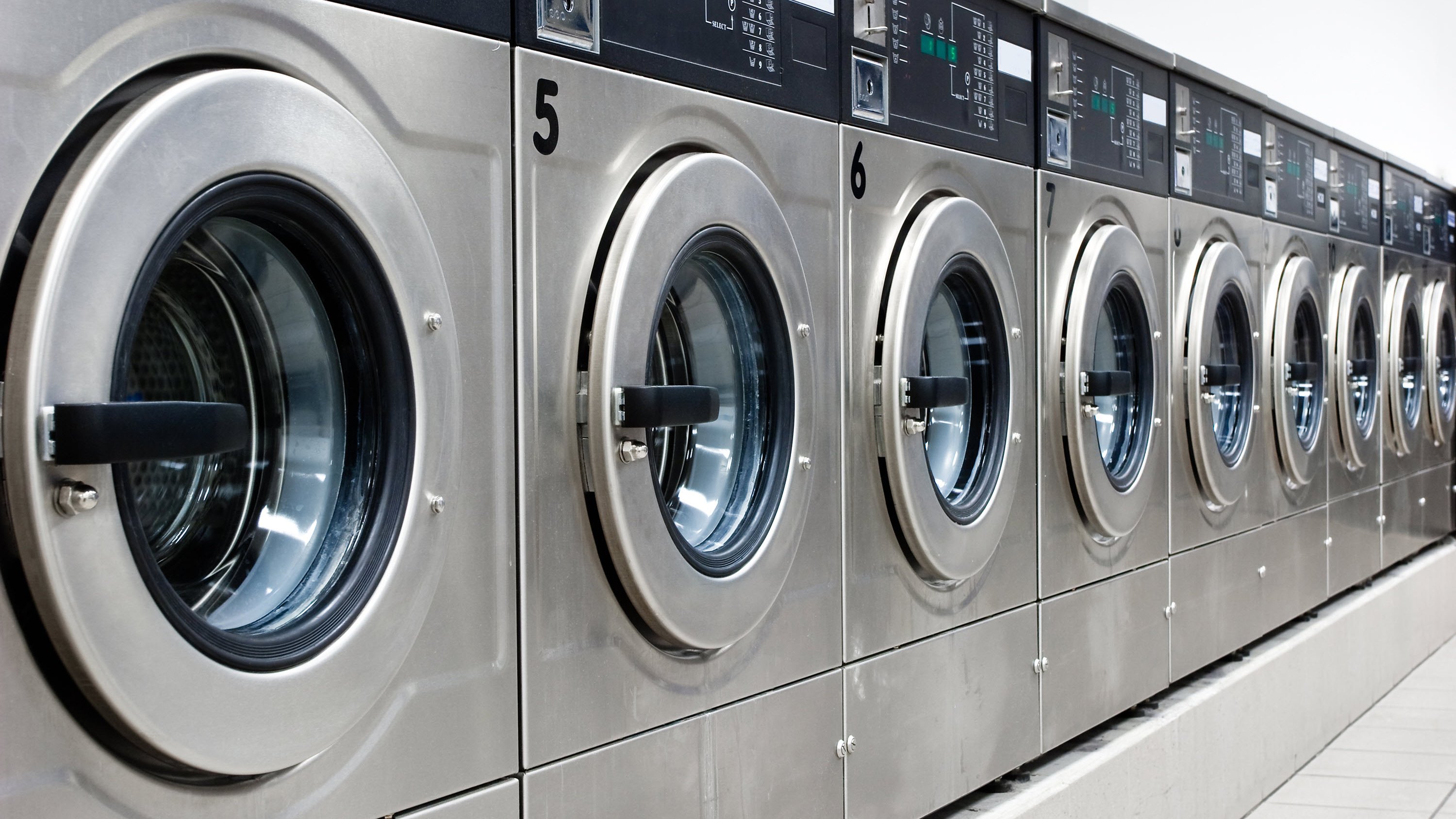 A row of stainless steel washing machines with digital displays and numbered dials.