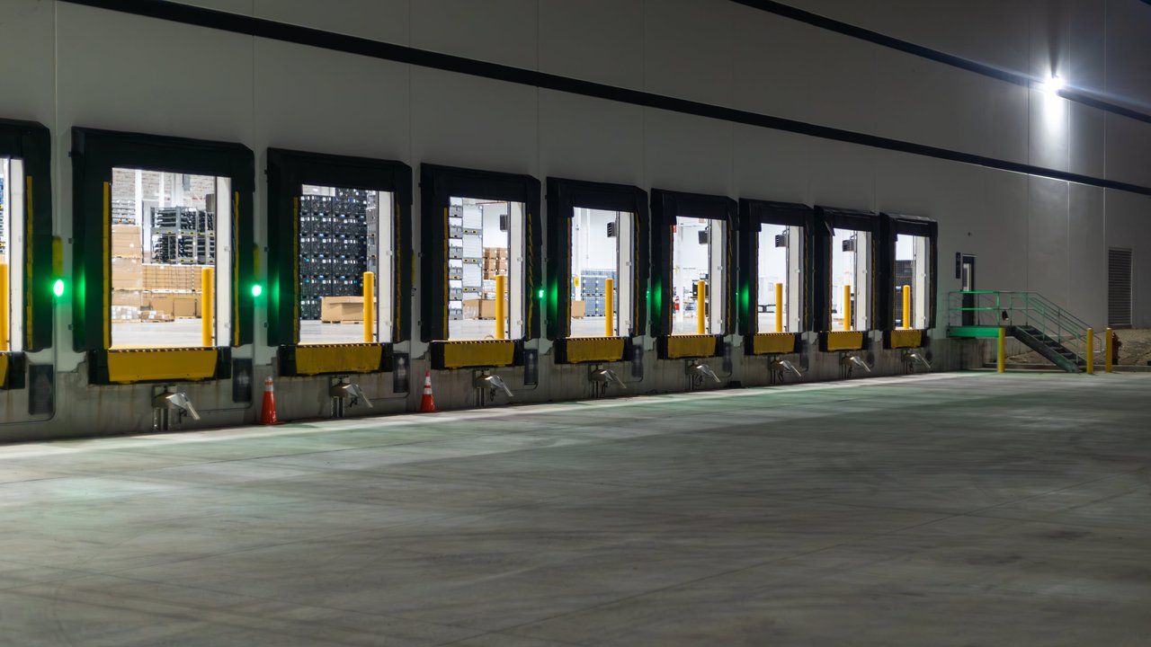 A row of loading docks with illuminated green lights at night, featuring open doors and a concrete area.