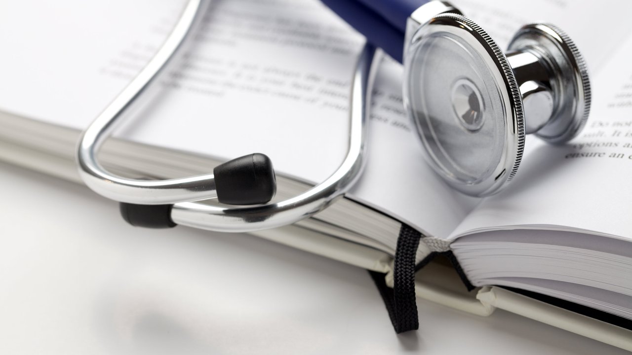 A stethoscope rests on an open book with visible text on the pages.