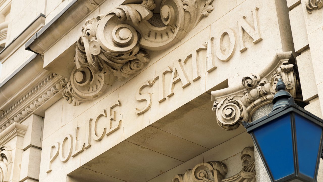 Close-up of a building facade with the words "POLICE STATION" and decorative stonework, featuring a blue lantern.