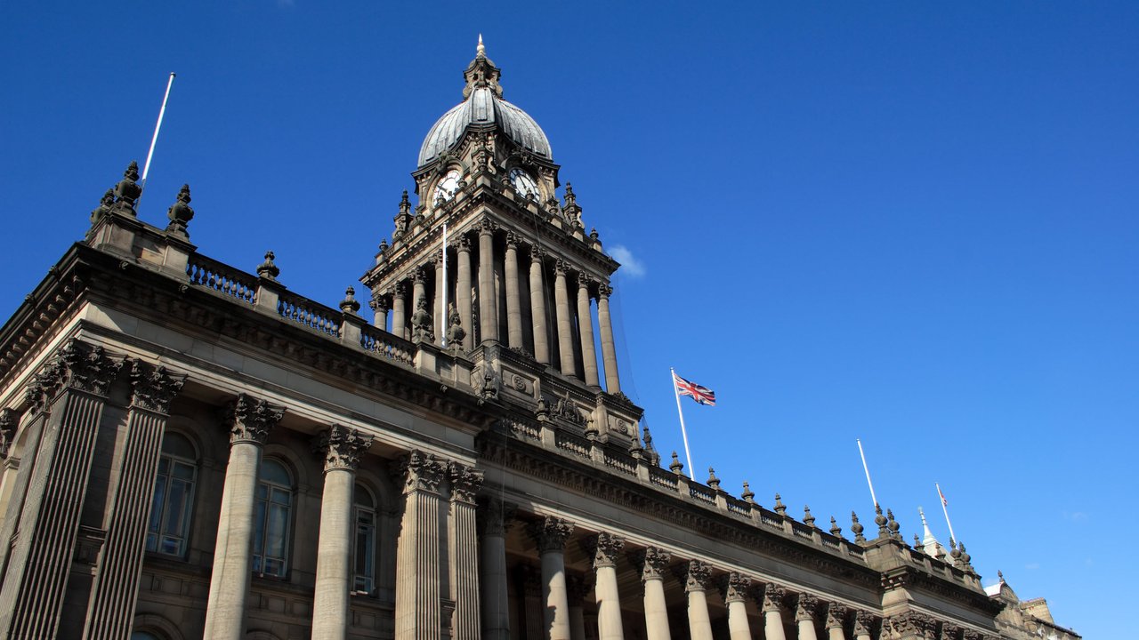 A historic building with a domed tower, columns, and a flag against a clear blue sky.