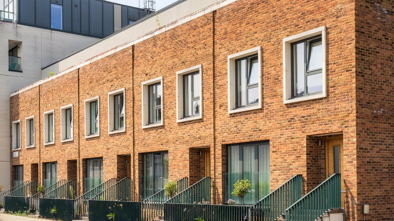 A row of modern brick houses with large windows and green railings, set against a clear sky.