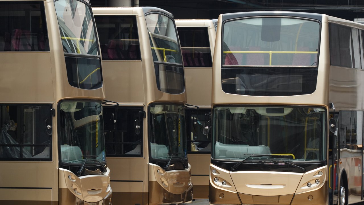 Four double-decker buses parked in a garage, showcasing their front and upper decks.