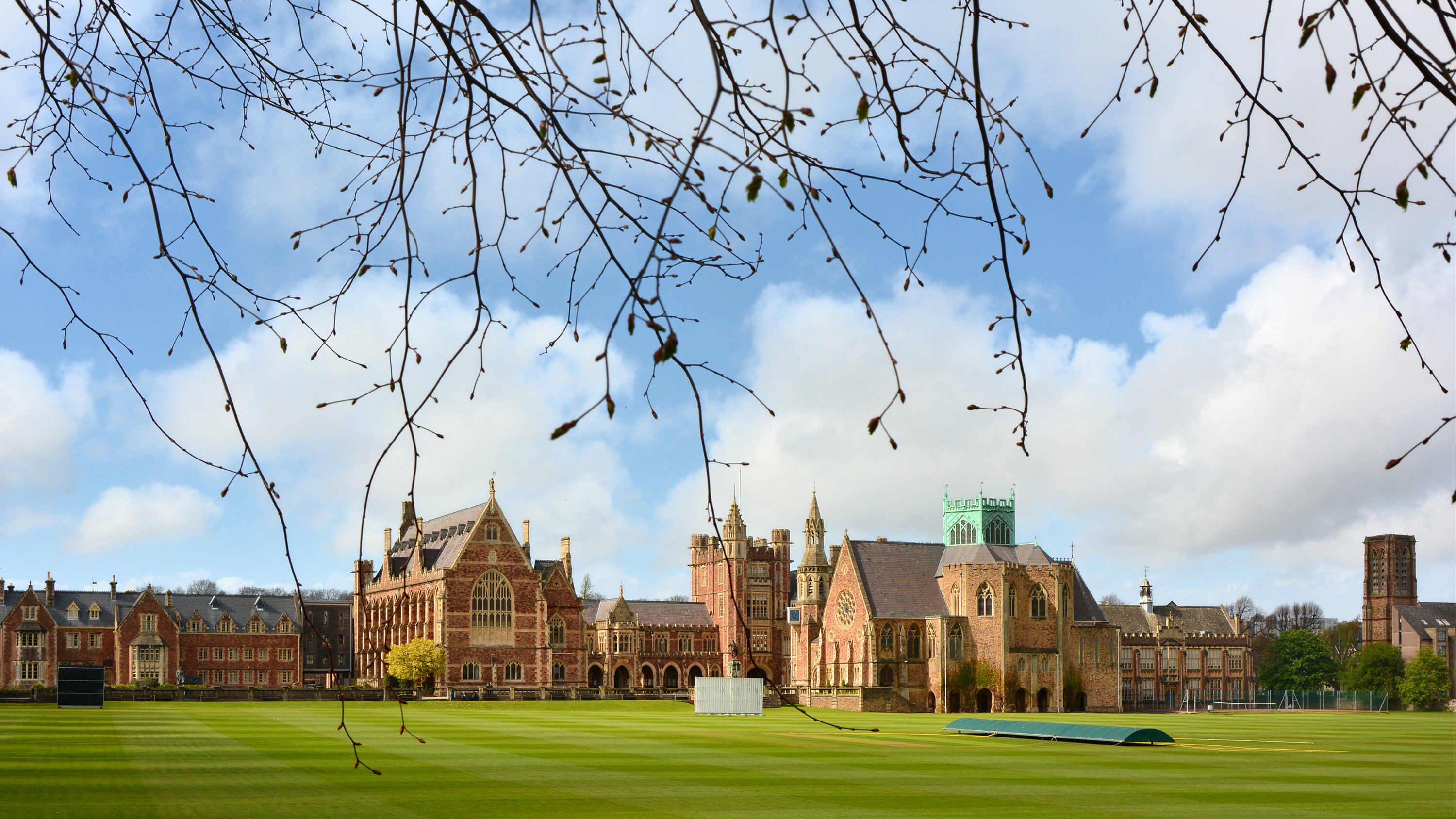 A historic campus with red brick buildings and a green lawn under a blue sky with scattered clouds.