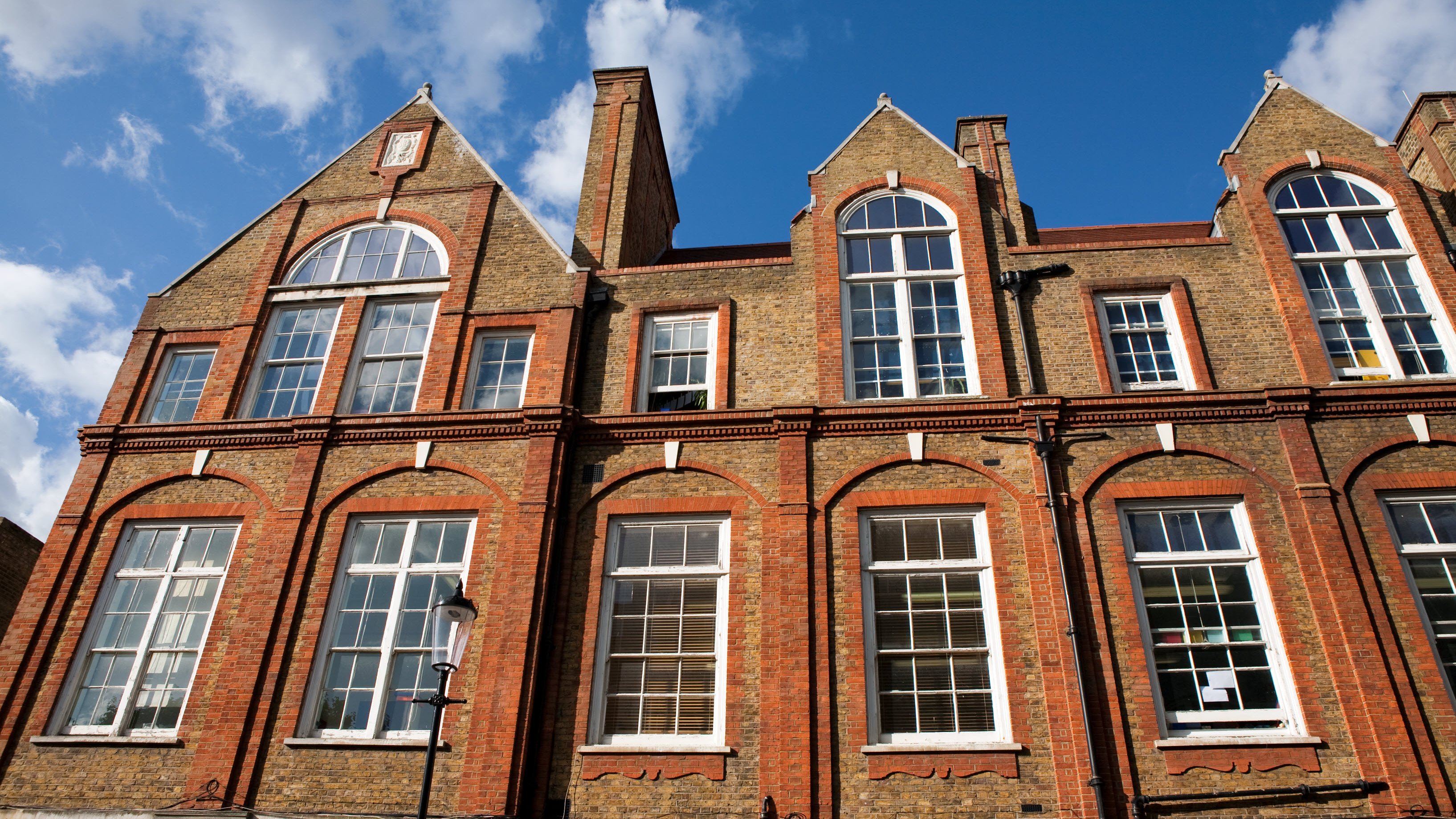 A brick building with large windows and a peaked roof against a blue sky with clouds.