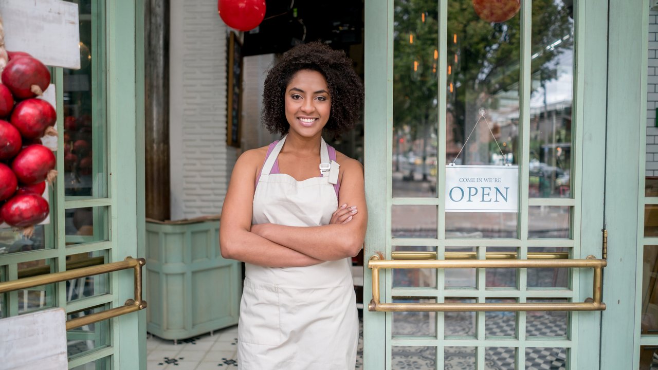 African American waitress standing at the door of a restaurant looking very happy with arms crossed