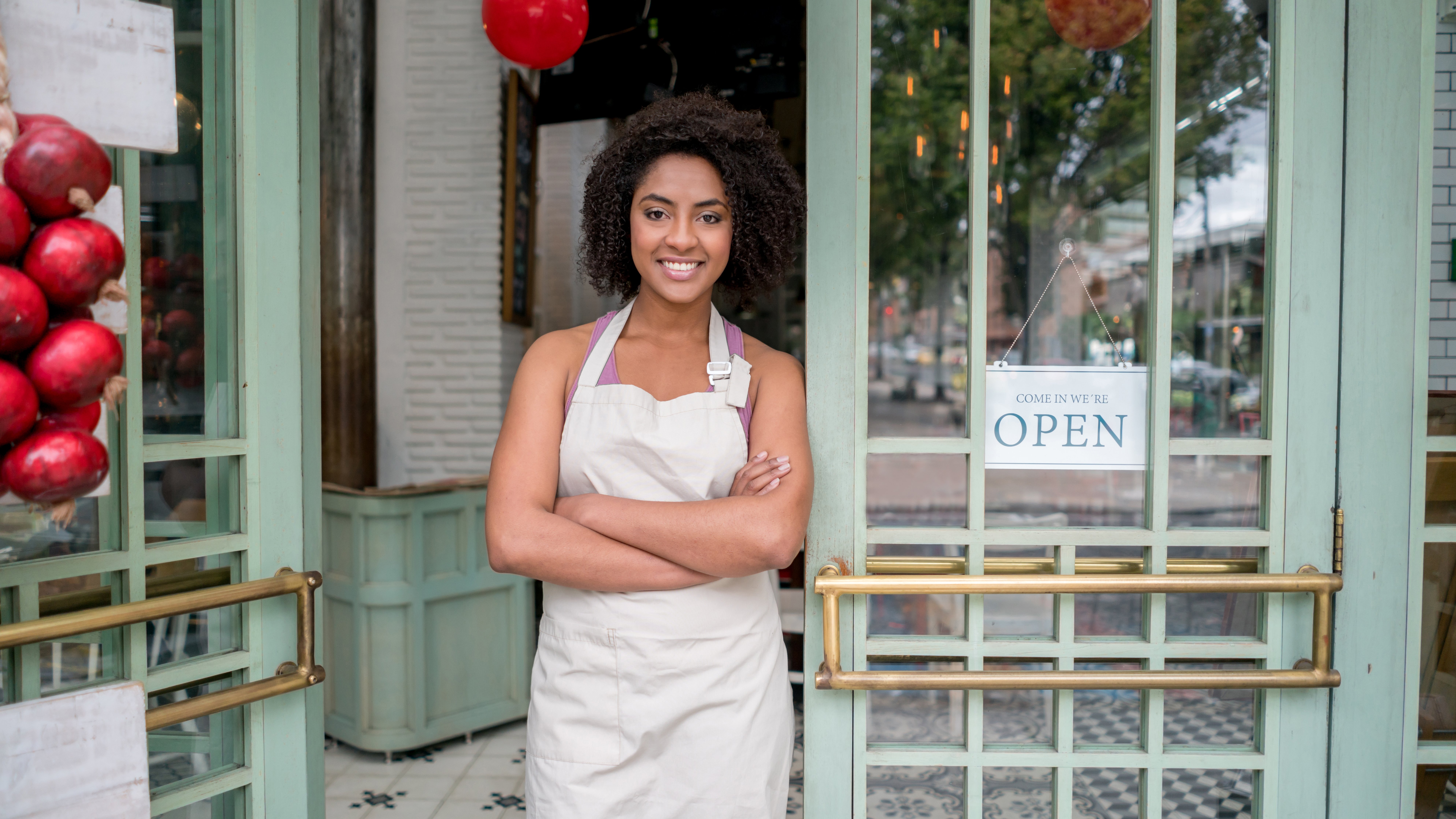 African American waitress standing at the door of a restaurant looking very happy with arms crossed