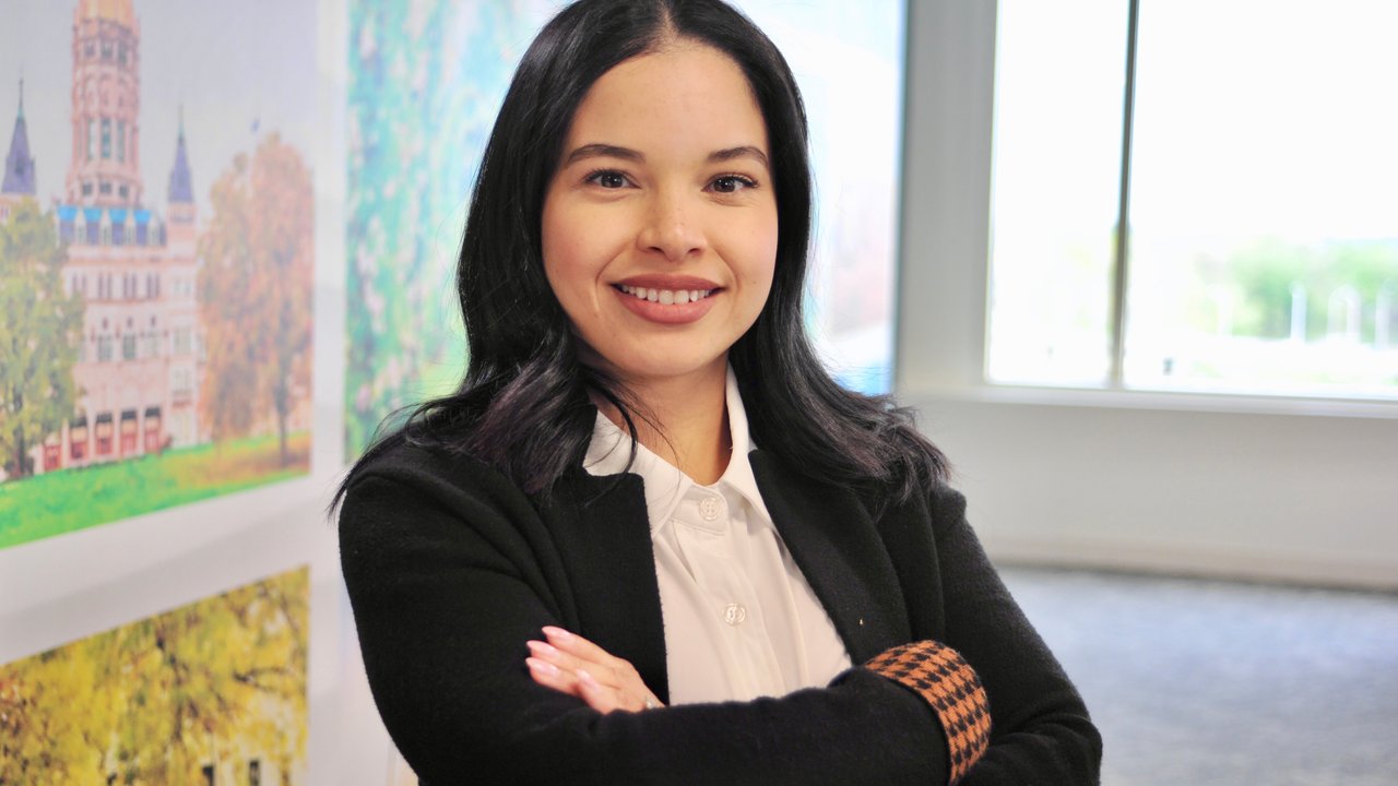 Early-career professional standing in sunny office smiling