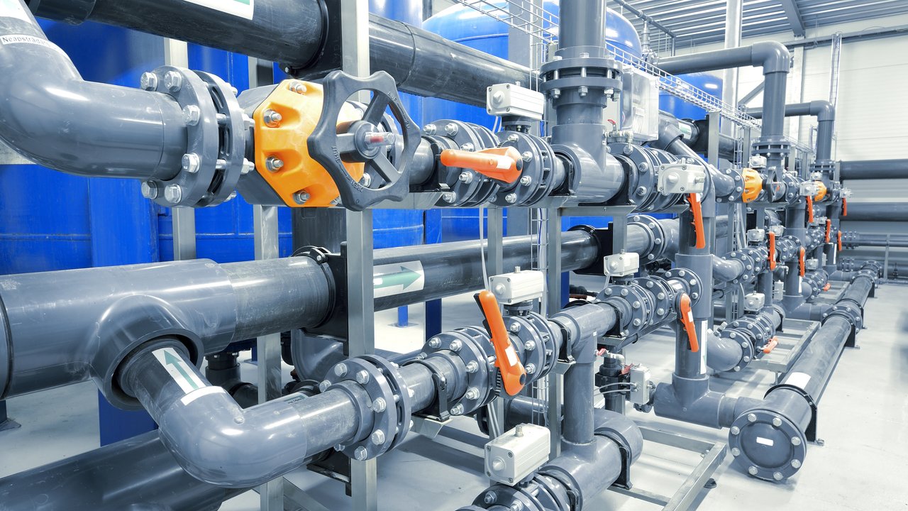 Large industrial water treatment and boiler room. Shiny steel metal pipes and blue pumps and valves.