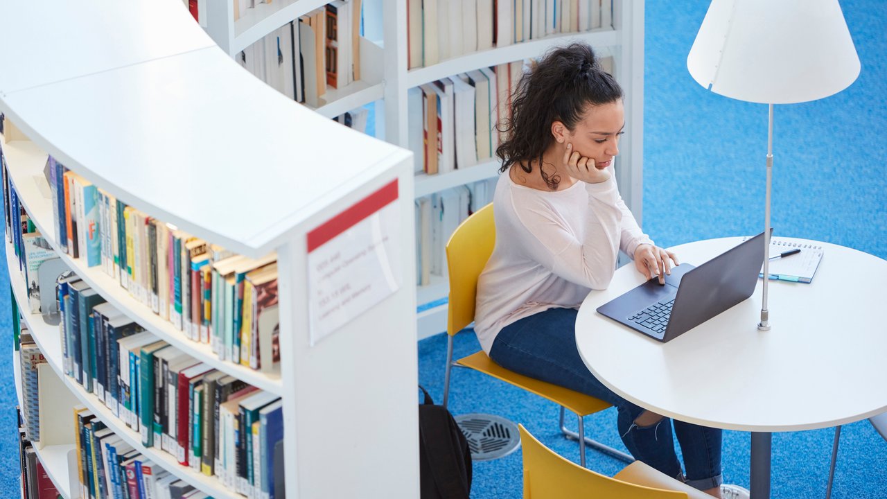 Young female adult reading laptop computer in library