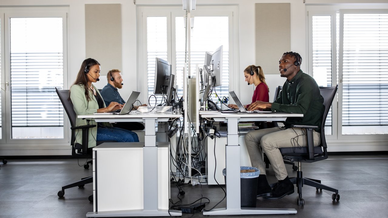 Group of help desk operators wearing headsets and working at their computers in a call center.