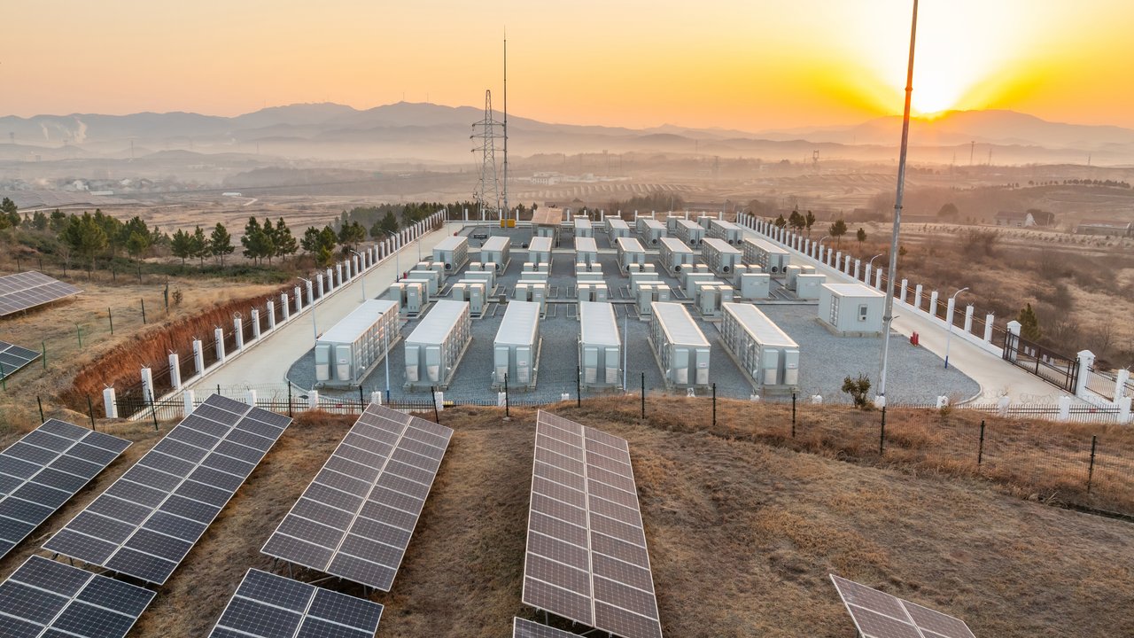 A solar energy facility with solar panels in the foreground and battery storage units in the background at sunset.