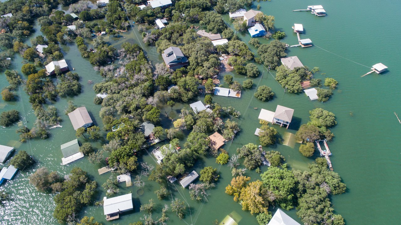 Aerial view of flooded residential area with houses and trees partially submerged in water.