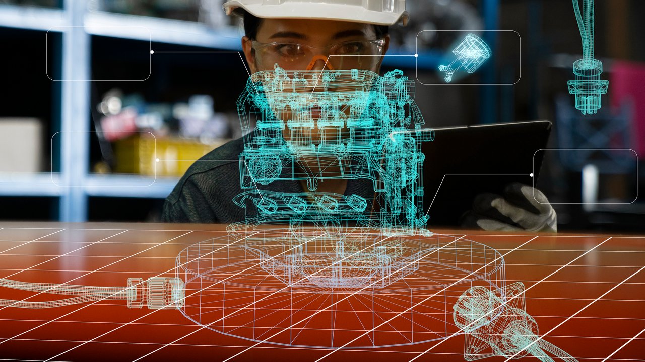 A person in a hard hat examines a tablet with a holographic engine model displayed above a work surface.
