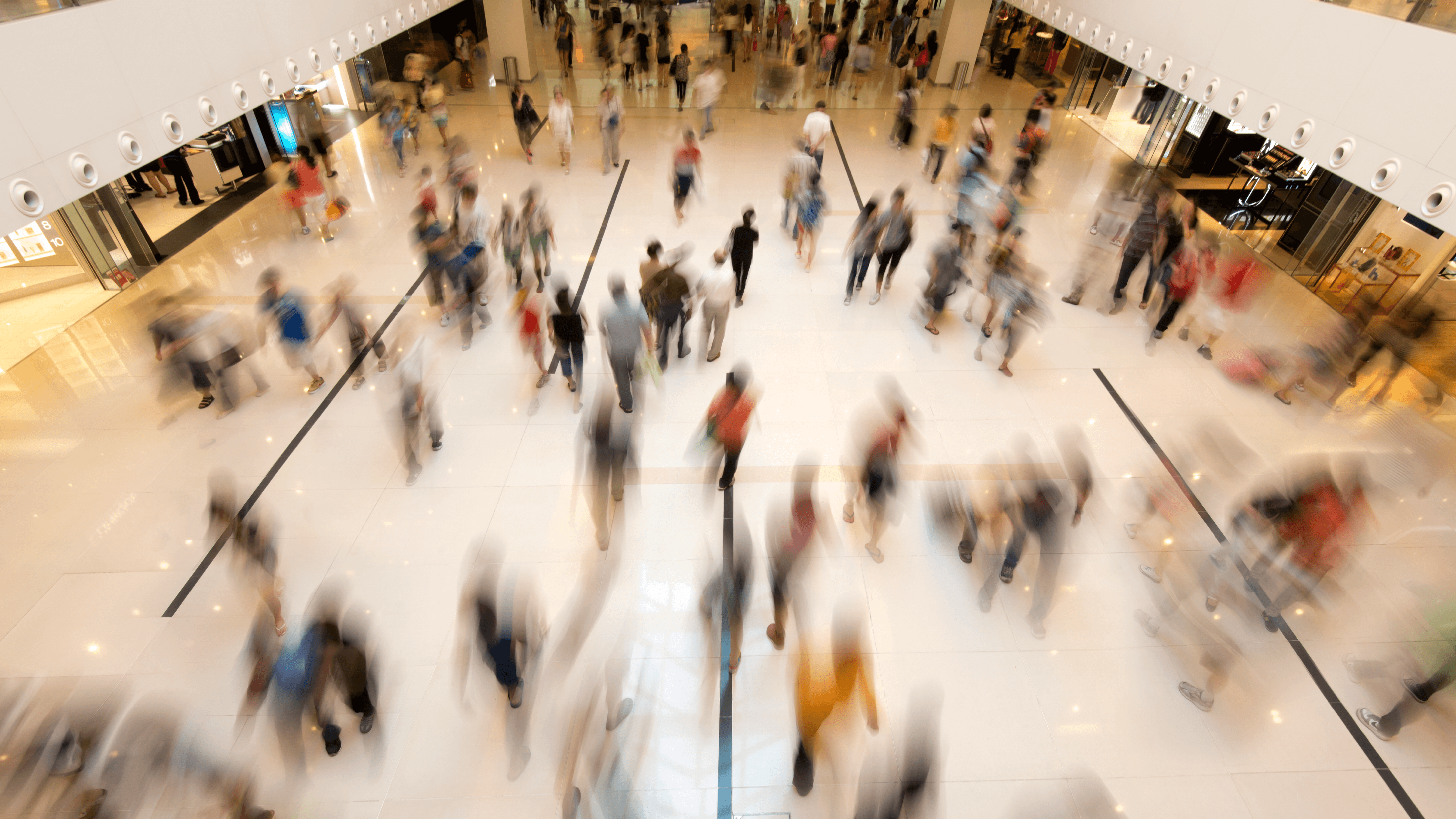 Une foule de personnes se déplace dans un grand espace commercial avec des boutiques en arrière-plan.