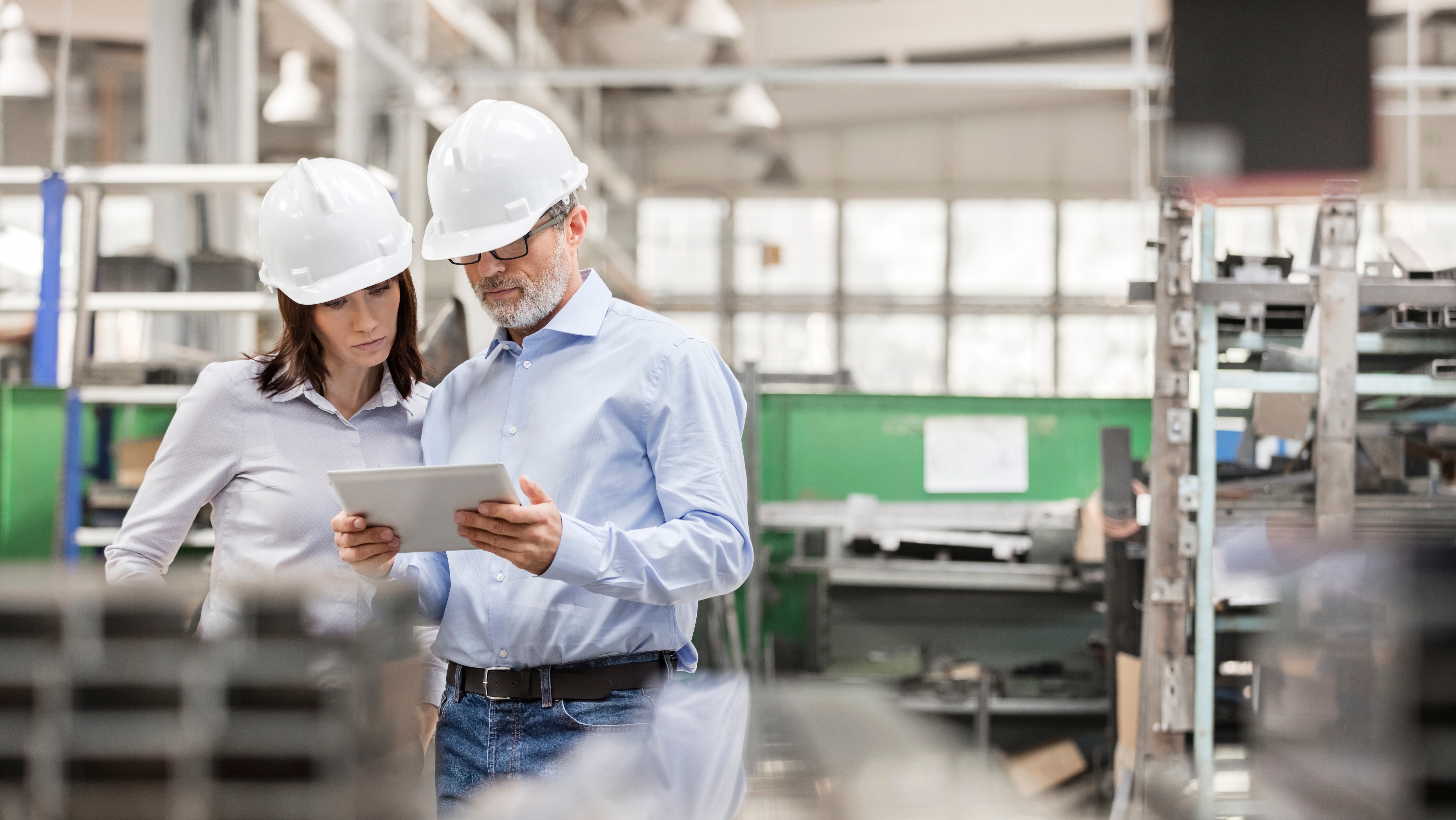 2 professionals wearing hard hats looking at tablet in industrial setting