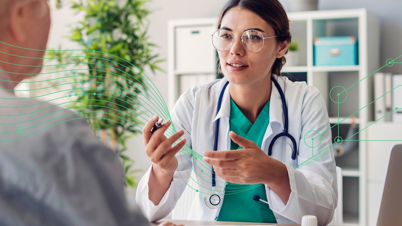 Female doctor wearing metal-framed glasses and stethoscope talking with hands to a patient in a medical office setting.