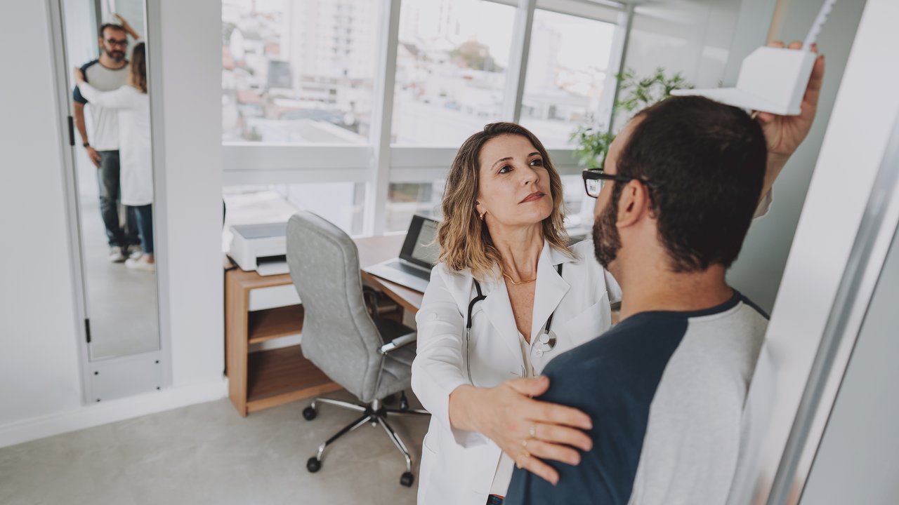 Portrait of a female doctor measuring a patient's height to calculate BMI