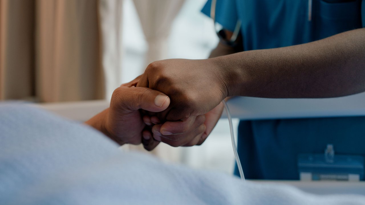 Nurse holding hands with patient under critical illness care
