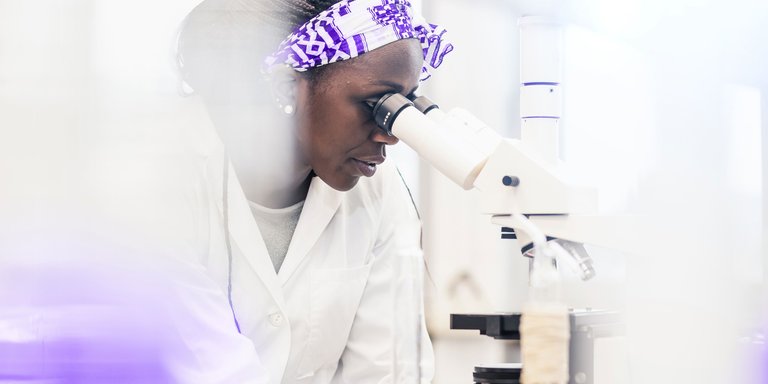 A person in a lab coat uses a microscope, surrounded by laboratory equipment and glassware.