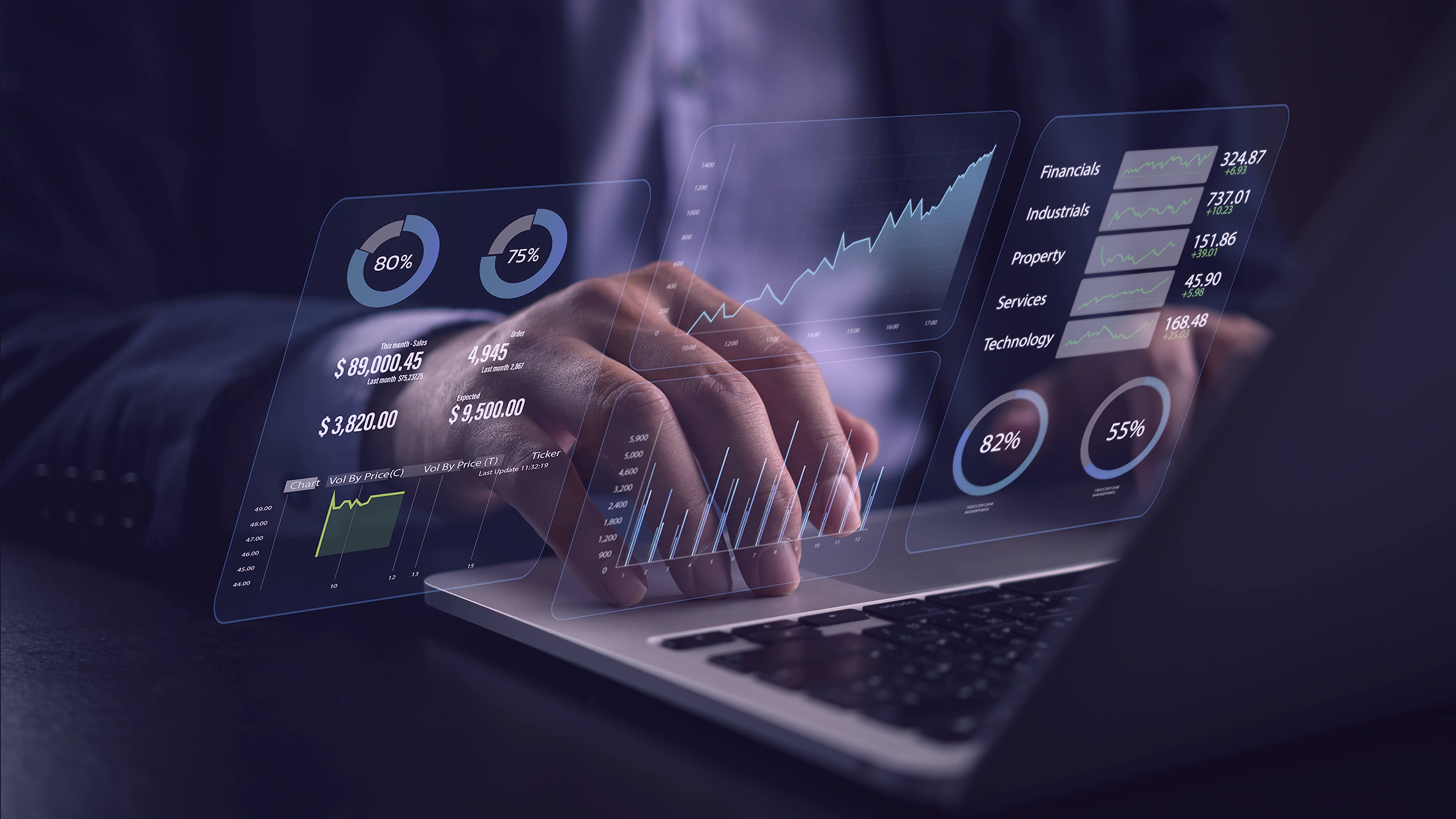 A person using a laptop with digital financial graphs and data displayed on the screen.