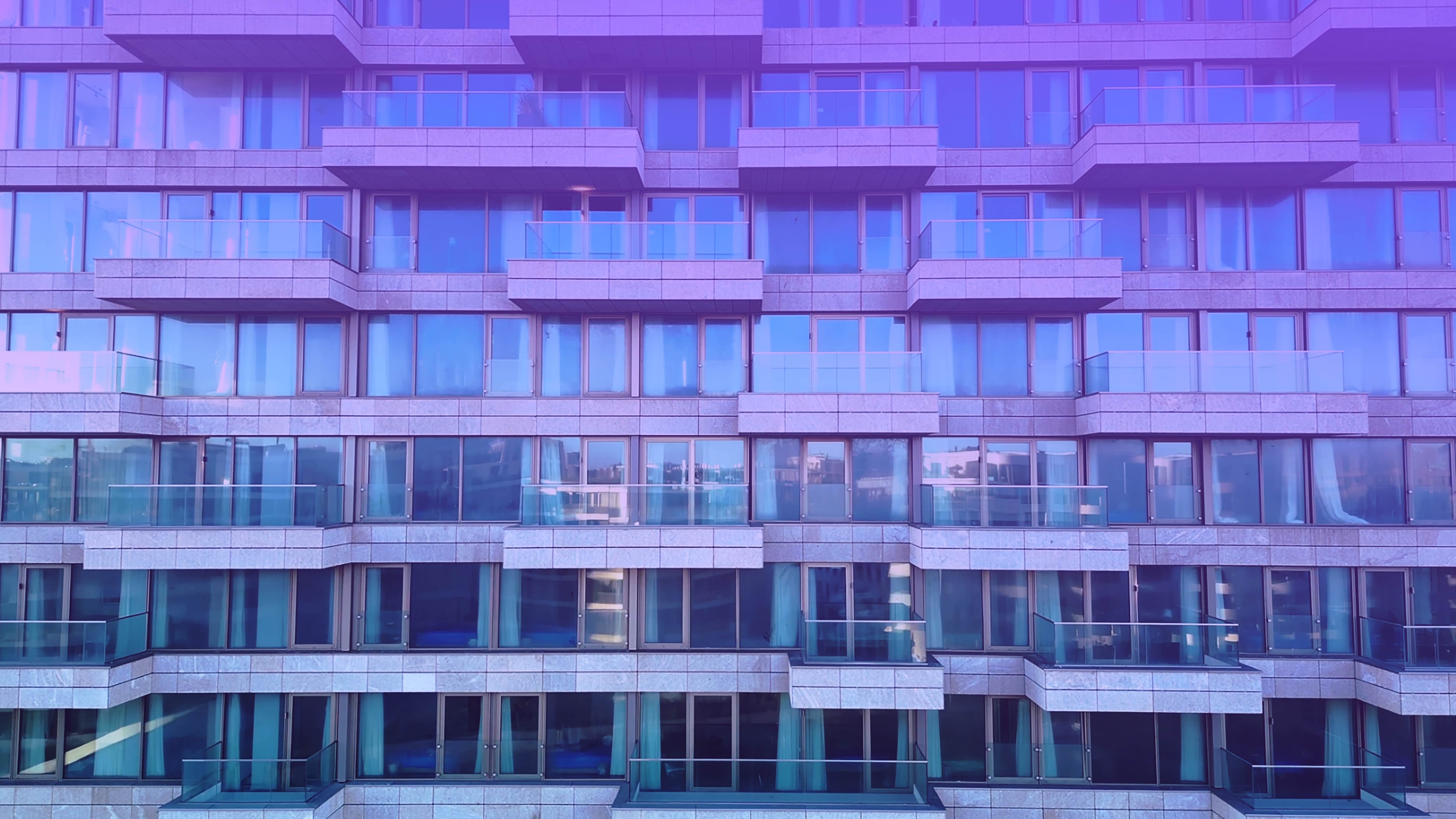 A modern building facade with multiple glass windows and balconies, featuring a purple tint.