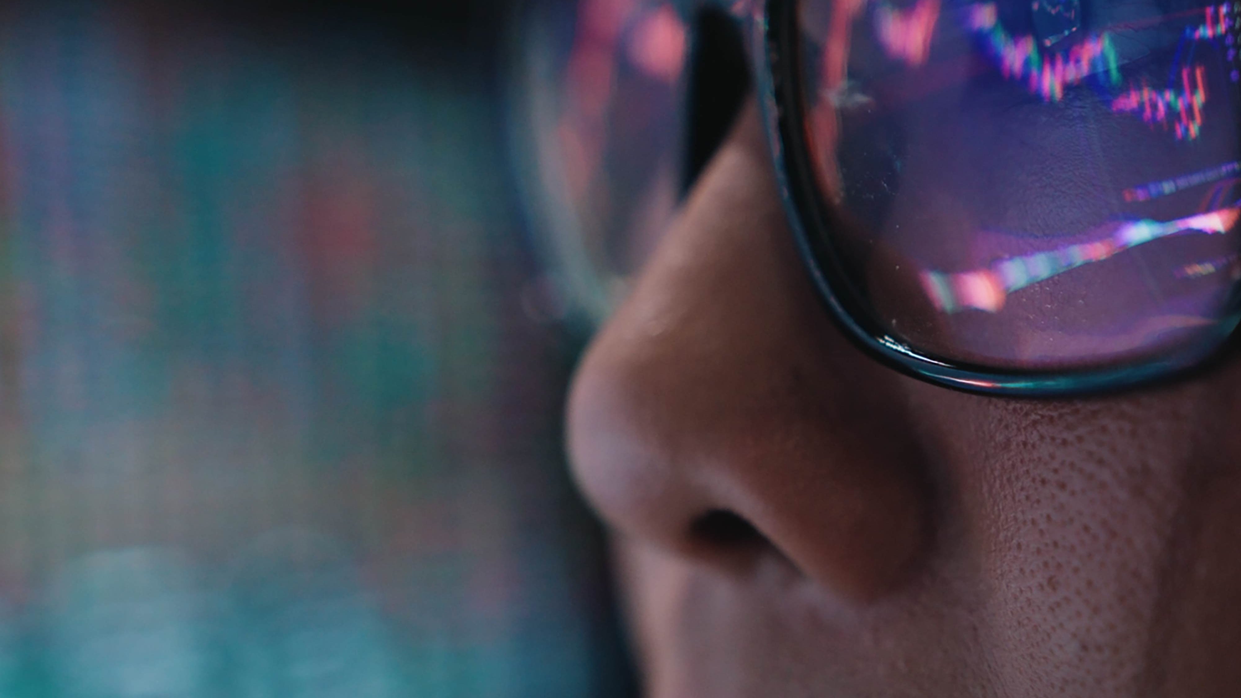 Close-up of a person's face wearing glasses, reflecting colorful stock market data on the lenses.