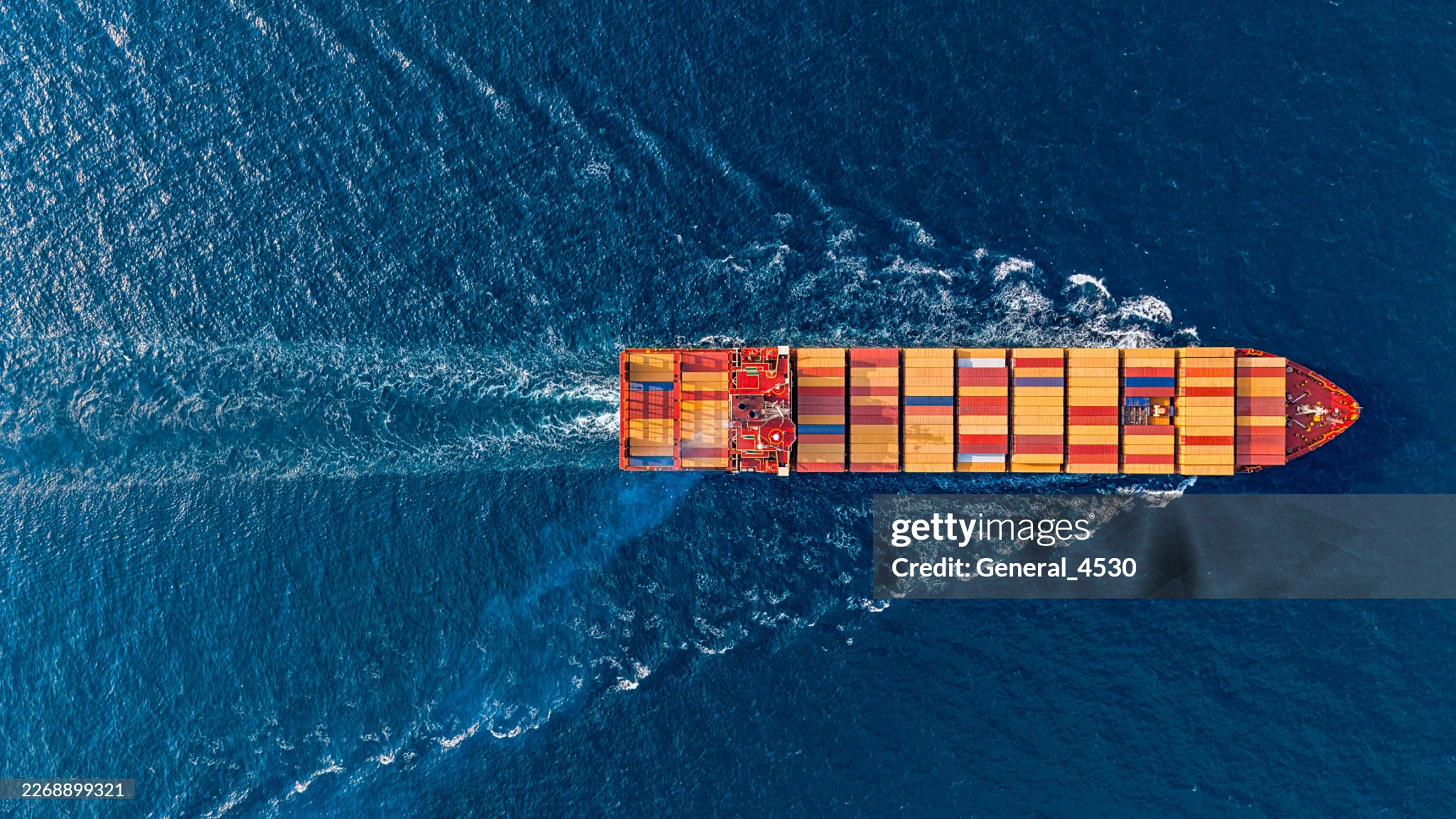 Aerial view of a large cargo ship with colorful containers sailing on deep blue ocean waters.