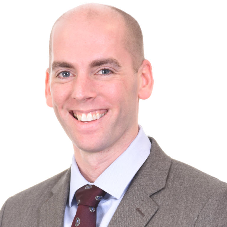 A smiling man with short hair, wearing a suit and tie, against a white background.
