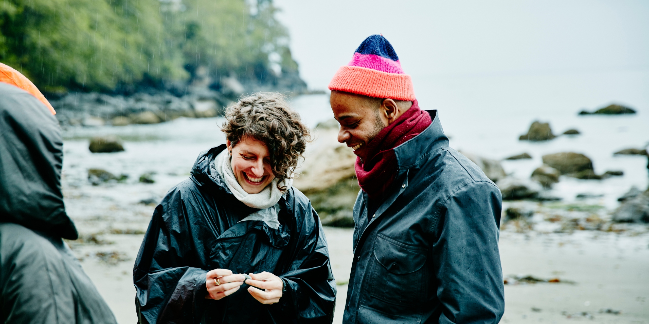 Smiling couple looking at rock found on beach during walk in rain