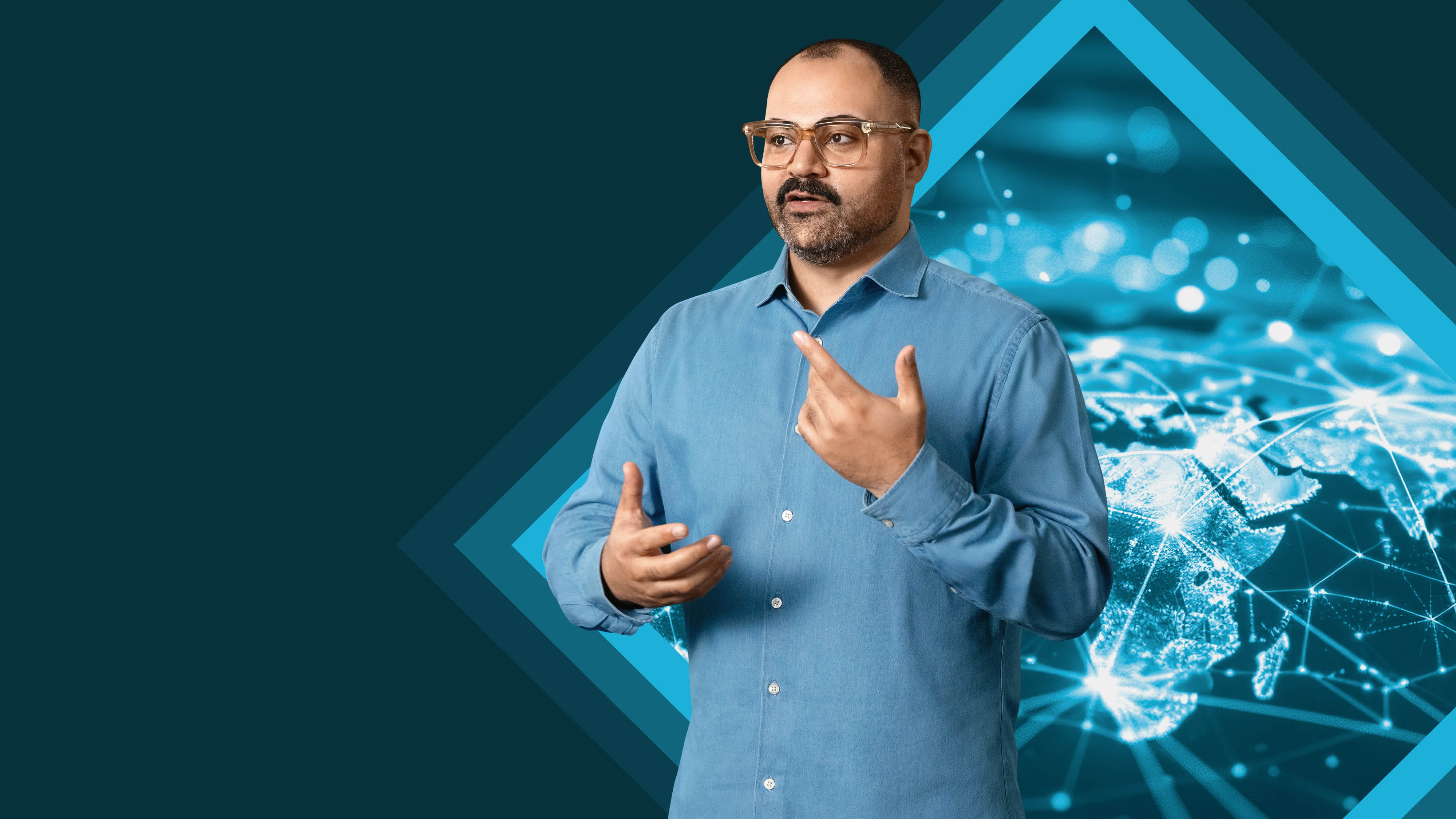 A man in a blue shirt gestures while speaking, with a digital network background.