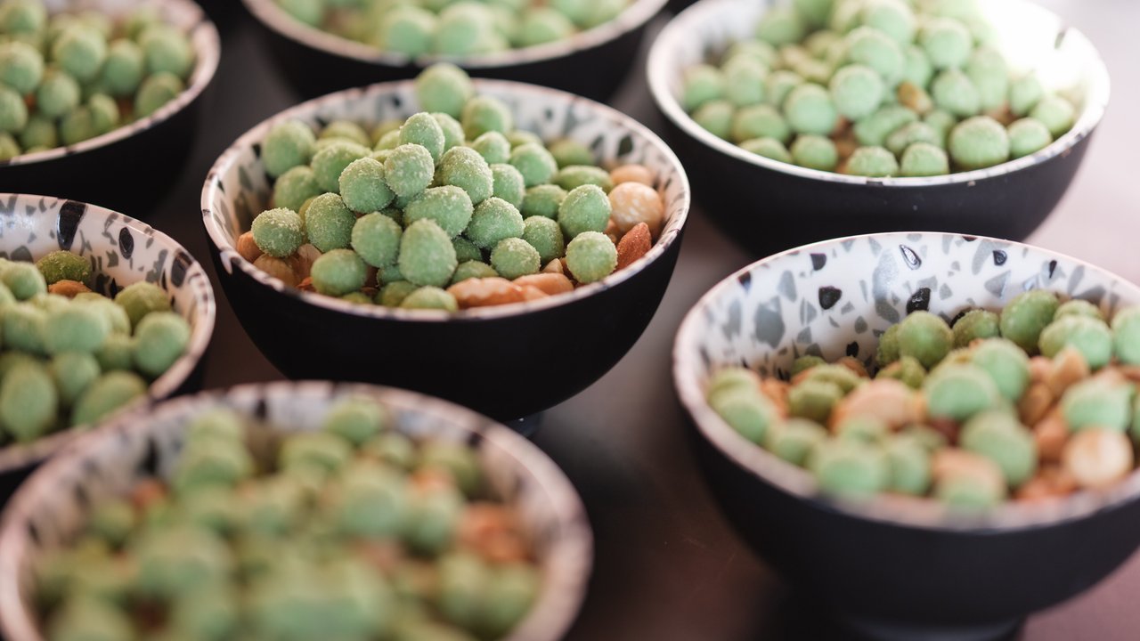 Several bowls filled with green snacks and nuts arranged on a dark surface.