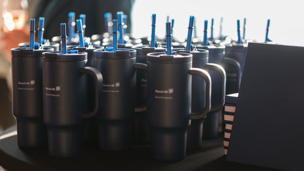 A table with multiple dark blue mugs featuring straws and a stack of notebooks beside them.