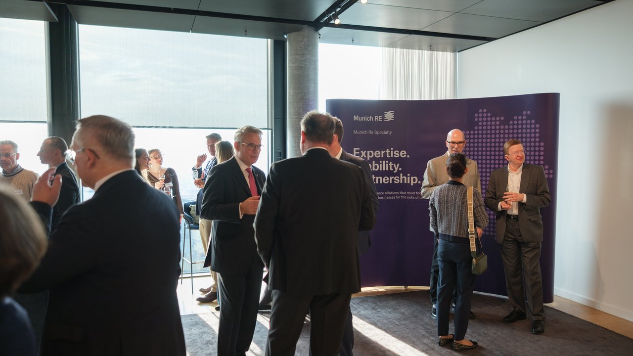 A group of professionals networking in a modern event space with a Munich Re banner in the background.